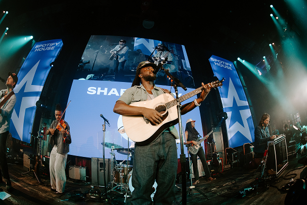 Shaboozey performing with his band, playing an acoustic guitar